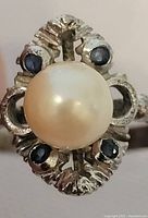 Close-up of the ring face showing the central large pearl with four small blue stones in ornate silver setting.