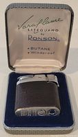 Vintage Ronson Varaflame lighter inside original fitted display case, showing satin printed lining and blue base.