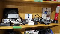 Shelf showing various electronic items including radios, power bank, Walkman, base station, alarm clock, flashlight, thermometer