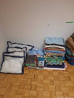 Multiple pillows with stuffing in plastic bags next to folded assorted fabrics and bedding