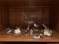 Shelf display with nine bird figurines including aluminum stylized birds, wooden carved birds, and a small glass bird figurine.