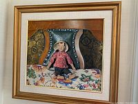 Framed painting showing seated figure on patterned cushion with detailed background and gold-toned frame.