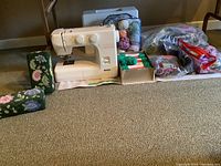 Full view of Kenmore sewing machine, wool yarn, sewing accessories, and two floral cross-stitch brick door stops arranged on carpet.