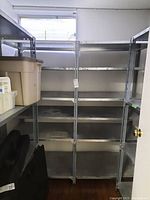 Two large metal shelving units joined together in basement next to window and door, empty besides some containers on side shelf.