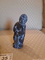Front view of soap stone figurine on beige textured couch with distinct facial and clothing details.