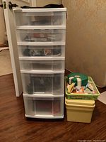 Full view of the tall plastic storage drawer unit alongside yellow and green storage containers with sewing supplies on hardwood floor