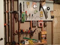 Wide shot of the pegboard with various hanging tools including saw, screwdrivers, file, and bungee cords along with accessory packs and boxes on wood shelves below.