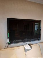 Front view of Sharp 52 inch LCD TV mounted on wall with remote control and owner's manual placed on couch below.
