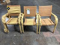 Three chairs side by side in warehouse setting; two outer chairs with paper-wrapped armrests and center armless chair