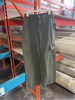 Front view of one pair of olive green cargo pants showing size tag, front pockets, cargo pockets, button, and zipper detail