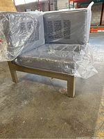 Front and side view of corner chair showing solid wood frame and cushioned seat and backrest wrapped in plastic.
