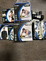 Pro Strength branded fitness equipment including ab wheels, resistance band sets, dumbbells, sauna suit, toning bands, and stretch cords arranged on floor.