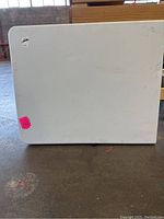 Full view of the white 4 foot folding table surface showing some scuff marks and a pink sale sticker.