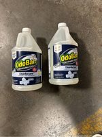 Two 1-gallon OdoBan disinfectant jugs on concrete floor showing front label.