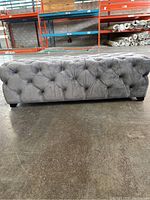 Side view of grey ruffed ottoman showing button tufting and fabric texture.