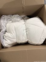 White duvet folded and placed inside an open cardboard box, showing smooth fabric and quilted sections.