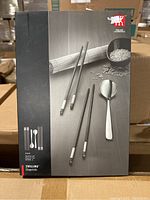 Front view of the sealed Zwilling chopstick set box showing the stainless steel chopsticks, dark chopsticks, and spoon illustration.
