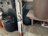 Full view of the boxed electric rotisserie kit leaning against a BBQ grill and other stored items, showing the packaging and partial product image.