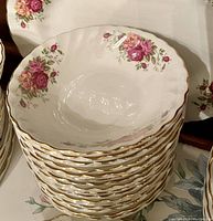 Stack of twelve white ironstone bowls with floral rose decorations and gold rim.