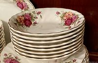 Stack of eight white ironstone bowls with rose floral pattern and gold rim detail.