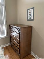 Angle view of the wooden dresser showing side and front, placed against beige walls on hardwood floor.