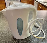 Front side view of white electric kettle showing shape, handle, cord and water level window.