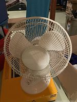 Front view of white table fan showing protective wire mesh grille and blades.