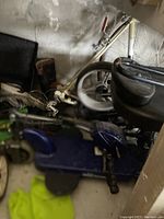 Photo showing the blue foldable scooter frame with black seat and folded position next to a bicycle wheel