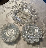 Top view of one large clear glass bowl with decorative petal/starburst edge design and three smaller bowls/plates arranged inside.