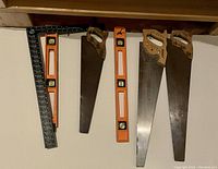Photo showing three wooden handled hand saws, two orange bubble levels, and one black metal carpenter's square
