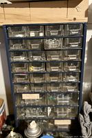 Blue metal hardware organizer with multiple clear plastic drawers containing assorted nails, screws, clips, and other small hardware items in used workshop condition.