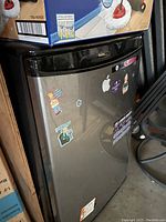Stainless steel Danby mini fridge with stickers on door in storage space