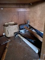 Wooden storage shelf containing three claw hammers with wooden or metal handles, a wood chisel, a metal plate, and a cardboard box with miscellaneous nails and screws.