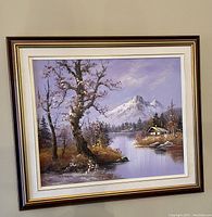 Framed oil painting of a mountain and lake landscape with trees and a small house.