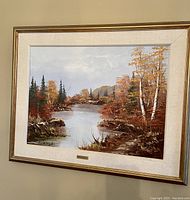 Full view of framed oil painting showing autumn river scene with trees and rocks.