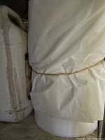 A close-up photo showing a large roll of white plastic bags tied with an elastic band, with a white cooler or similar container next to it.