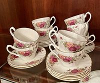 Nine white ironstone tea cups and nine matching saucers, all decorated with the Rose Garden floral pattern by Myott. Pieces have a gold trim and detailed rose designs.