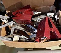 Box filled with multiple red and gray metal shelf brackets and hardware pieces showing general used condition
