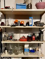 Wooden shelf with multiple jars, boxes, and tools including manual hand drill, tape measure, nails, screws, and metal containers