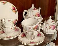 Photo showing teapot with lid, sugar bowl with lid, creamer, 4 tea cups stacked and 4 saucers with floral Rose Garden pattern.