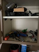 Hand tools and accessories inside a cabinet, including screwdrivers, wrenches, flashlight, and plastic containers.