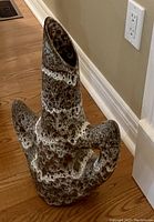 Photo of a uniquely shaped ceramic vase with multiple openings and textured brown and beige speckled surface placed on a wooden floor near a wall outlet.