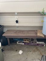 Long brown wooden bench shown under garage door with some dirt and objects on and near it