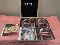 Five CD cases showing classic rock and roll, classic hits, and women in song collections on a pink cloth.