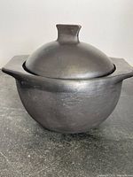 Angle view of black clay Chamba pot with lid sitting on a grey surface