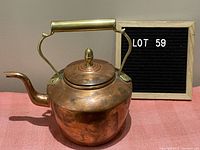 Side angle photo showing the kettle's curved spout and patina on copper body with brass handle and lid knob