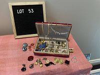 Photo of costume jewelry collection arranged on a pink fabric surface and inside an open jewelry box, with a letter board labeled 'LOT 53'.