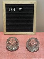 Pair of small round crystal taper candle holders with intricate cut design, displayed on pink fabric with Lot 21 sign behind.