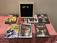 Lot 75 with seven DVDs arranged in two rows on a pink surface, including movies and video games.