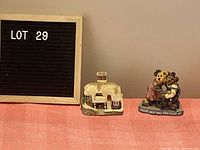 Two figurines displayed side by side: a Bearstone Sisters bear figurine and a small house figurine.